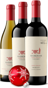 Three bottles of Markham Vineyards wine: one white and two red. Classic red glass Holiday ornament in front of them.
