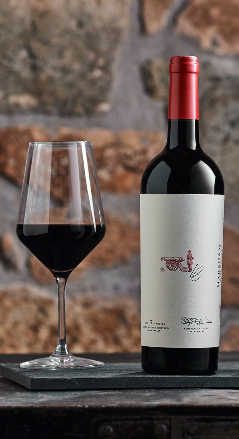 Bottle of Marked Parcels Cabernet next to a red wine glass with stone background