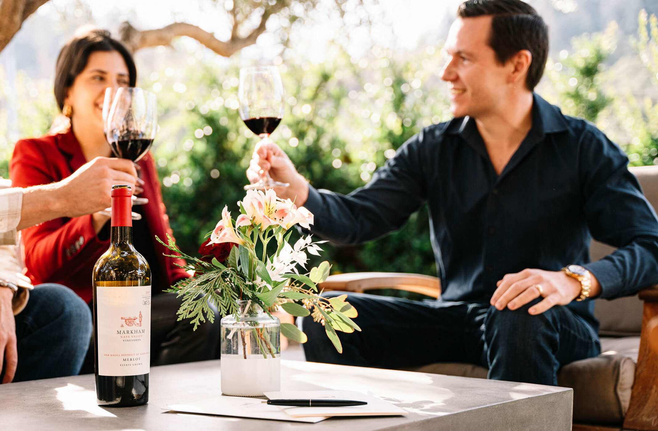 people toasting red wine glasses with bottle of Markham Merlot on table
