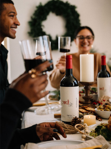 Holiday table setting with markham wine bottle and people drinking red wine