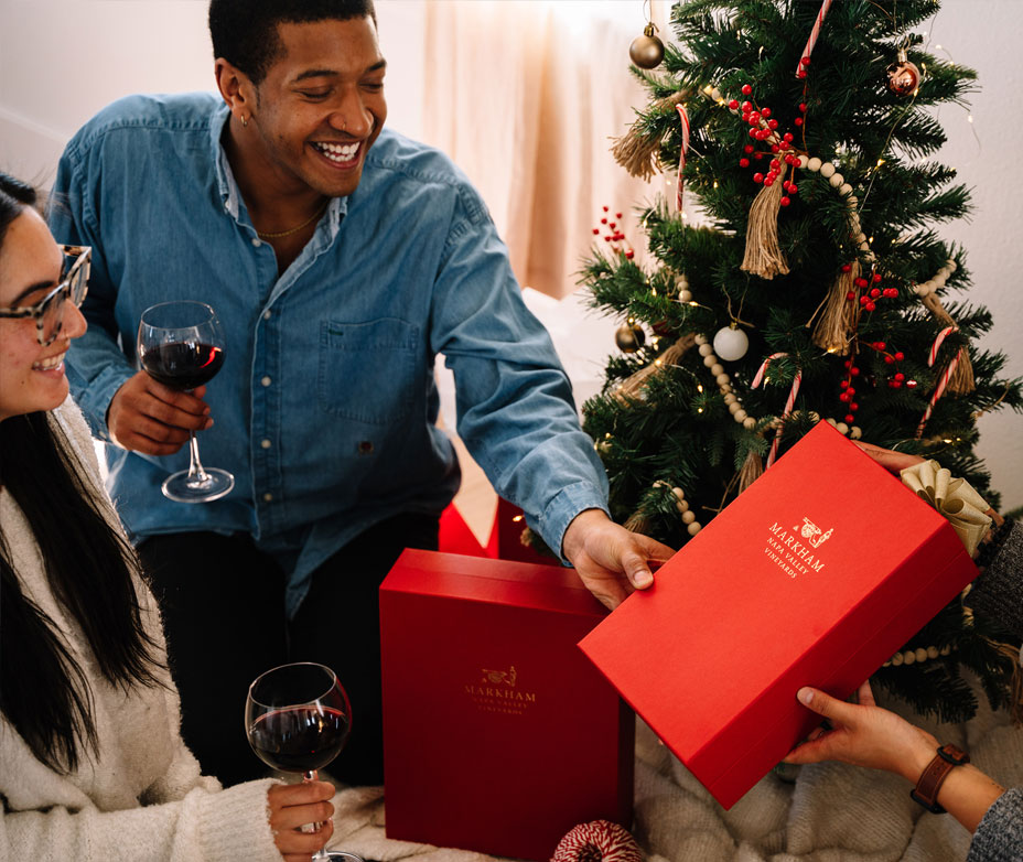 man handing over red gift box in front of holiday tree