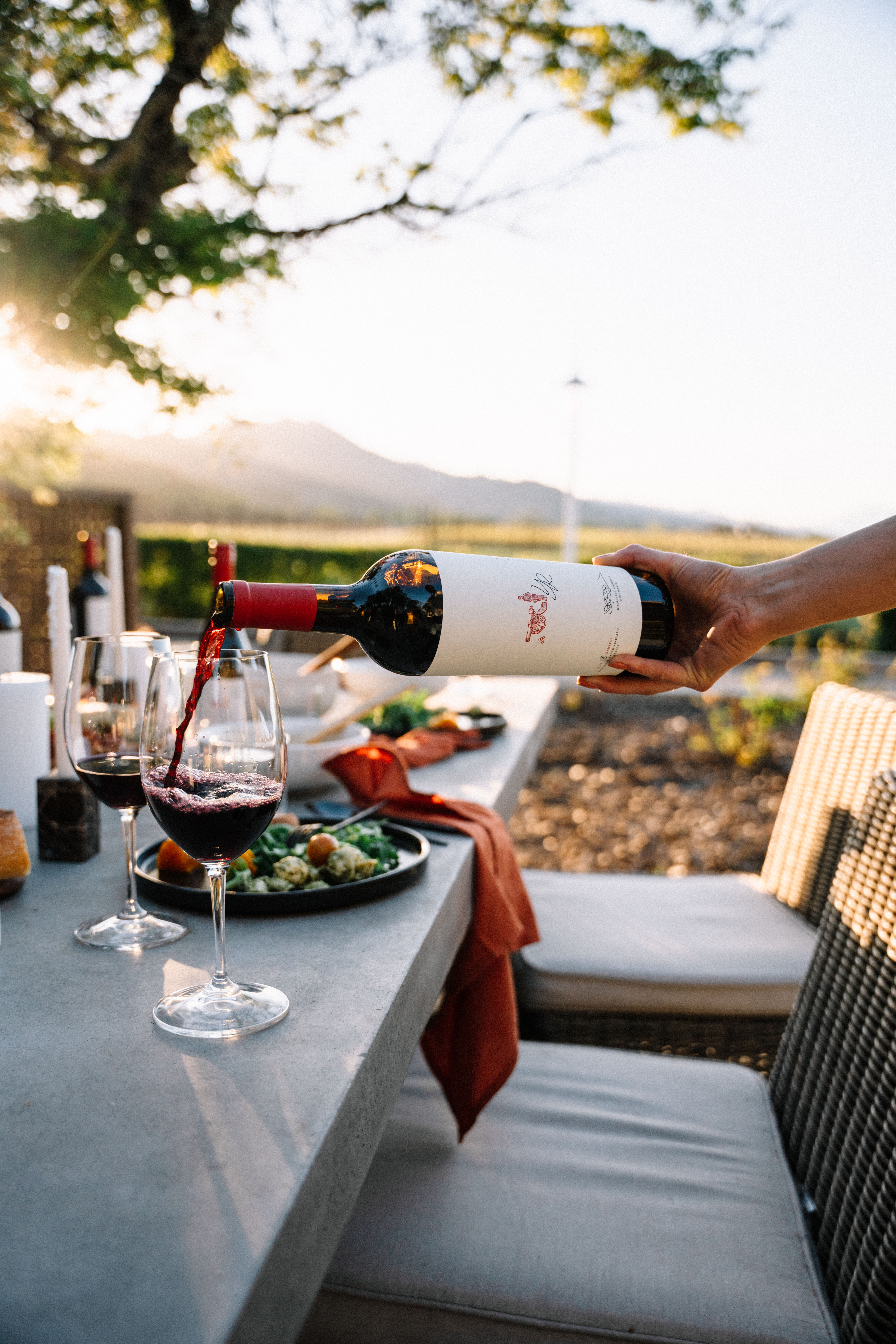 Red wine being poured into a glass with food on a table in the background.