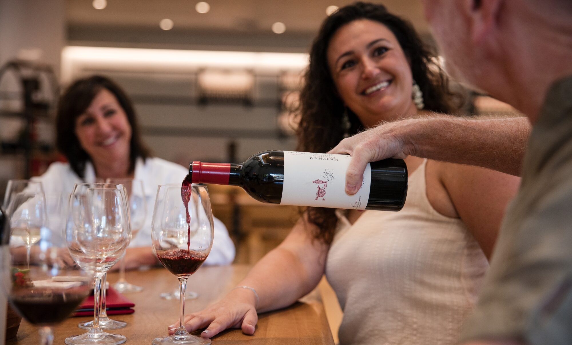 Person pouring a glass of Markham wine at a table in the Markham tasting room.